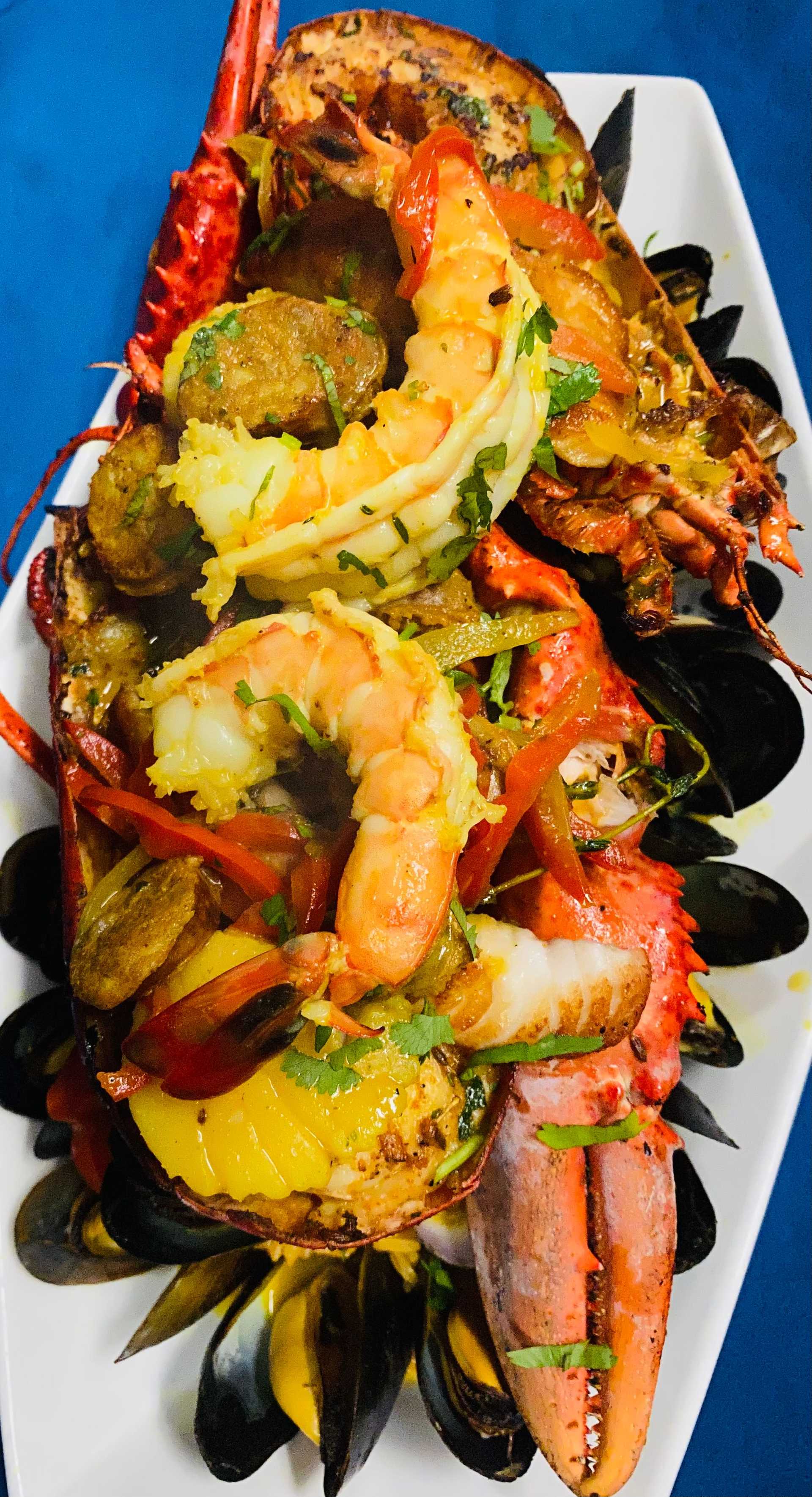 A gourmet seafood platter featuring lobster, shrimp, mussels, and various garnishes on a white plate.