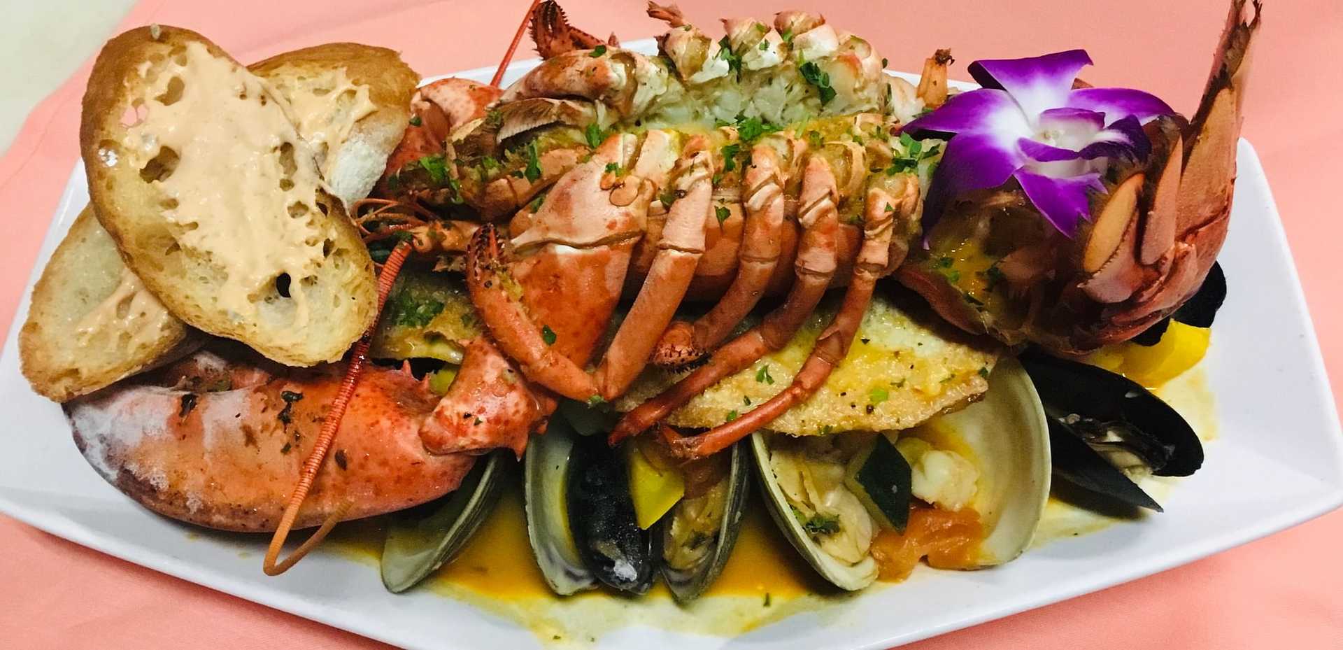 Seafood platter with lobster, clams, mussels, fish, and toasts, garnished with a purple orchid.