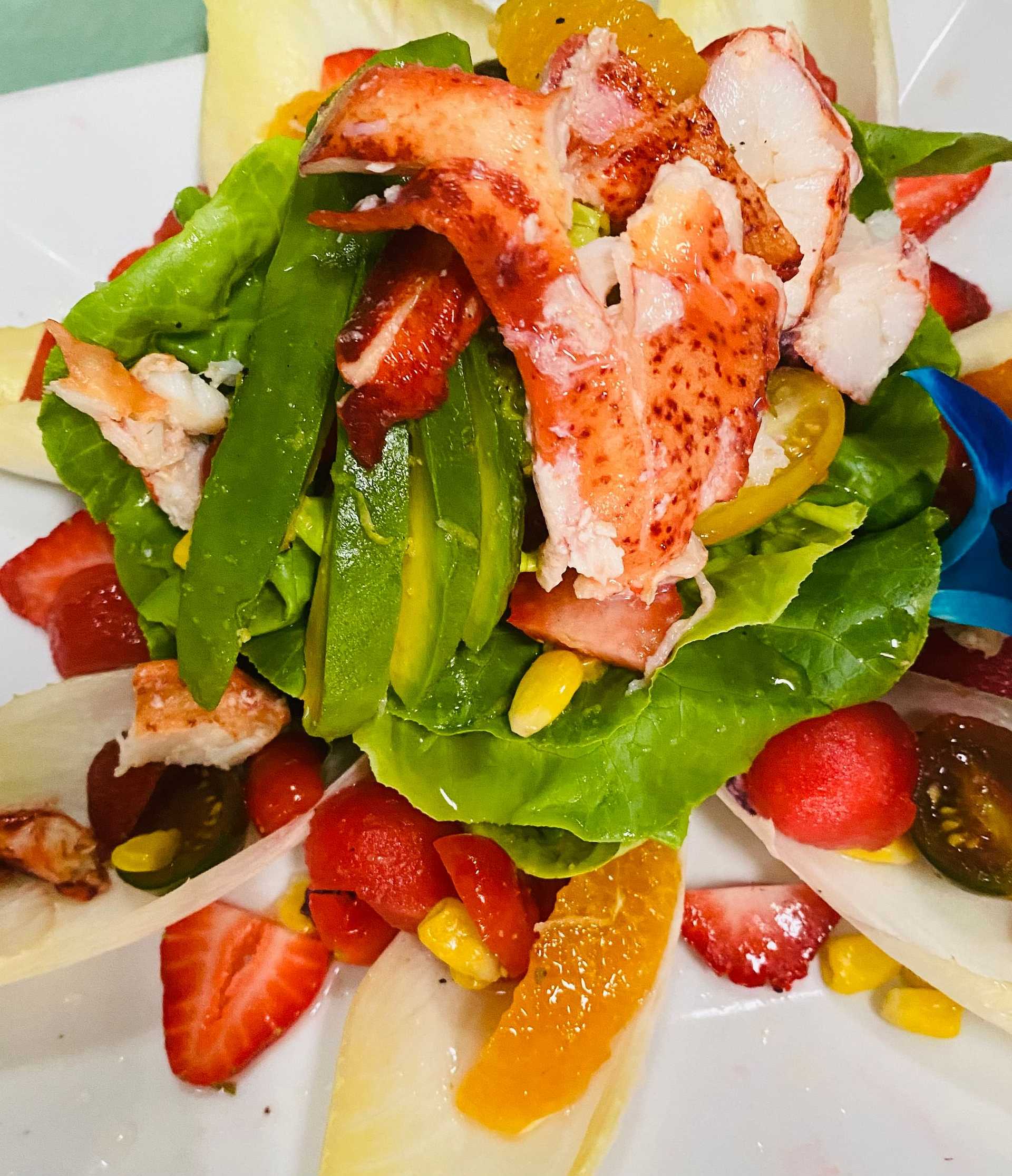 Colorful seafood salad with lobster, avocado, strawberries, and assorted fresh vegetables on a plate.