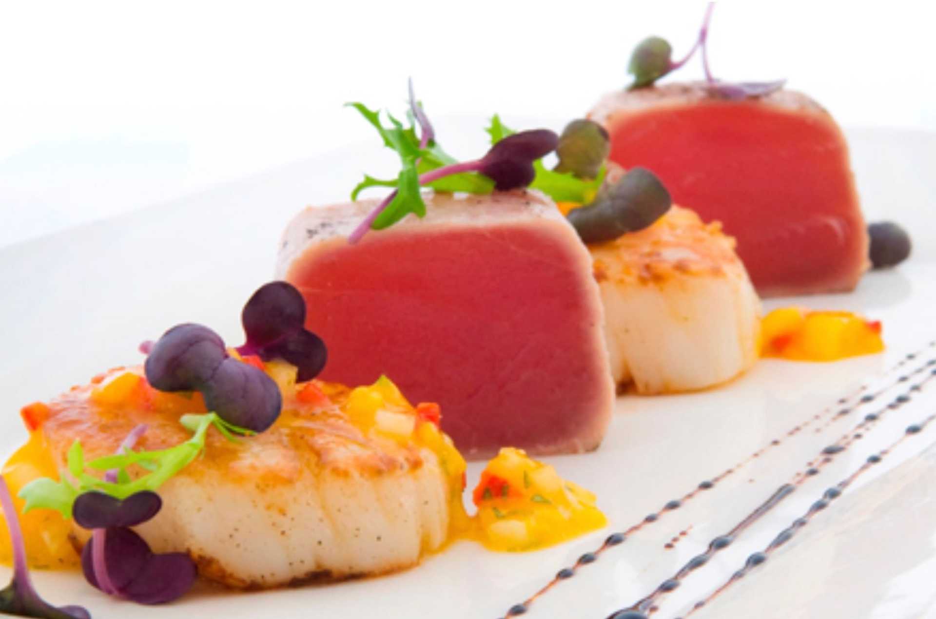 Gourmet dish with seared tuna, scallops, microgreens, and a drizzle of sauce on a white plate.