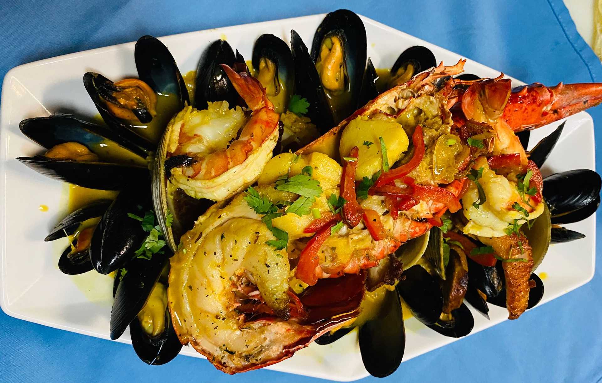 Plated seafood dish with cooked lobster, shrimp, and mussels garnished with herbs and sliced vegetables.